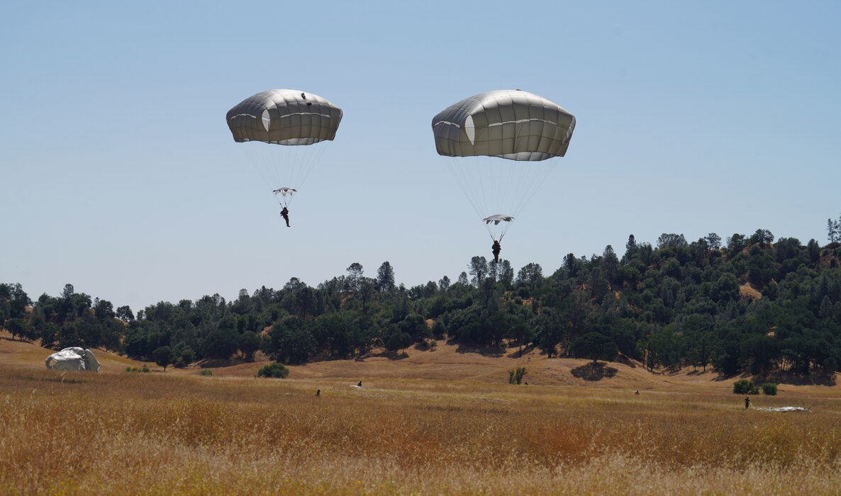 A photo of U.S. Army Paratroopers about to land on a grassy knoll.