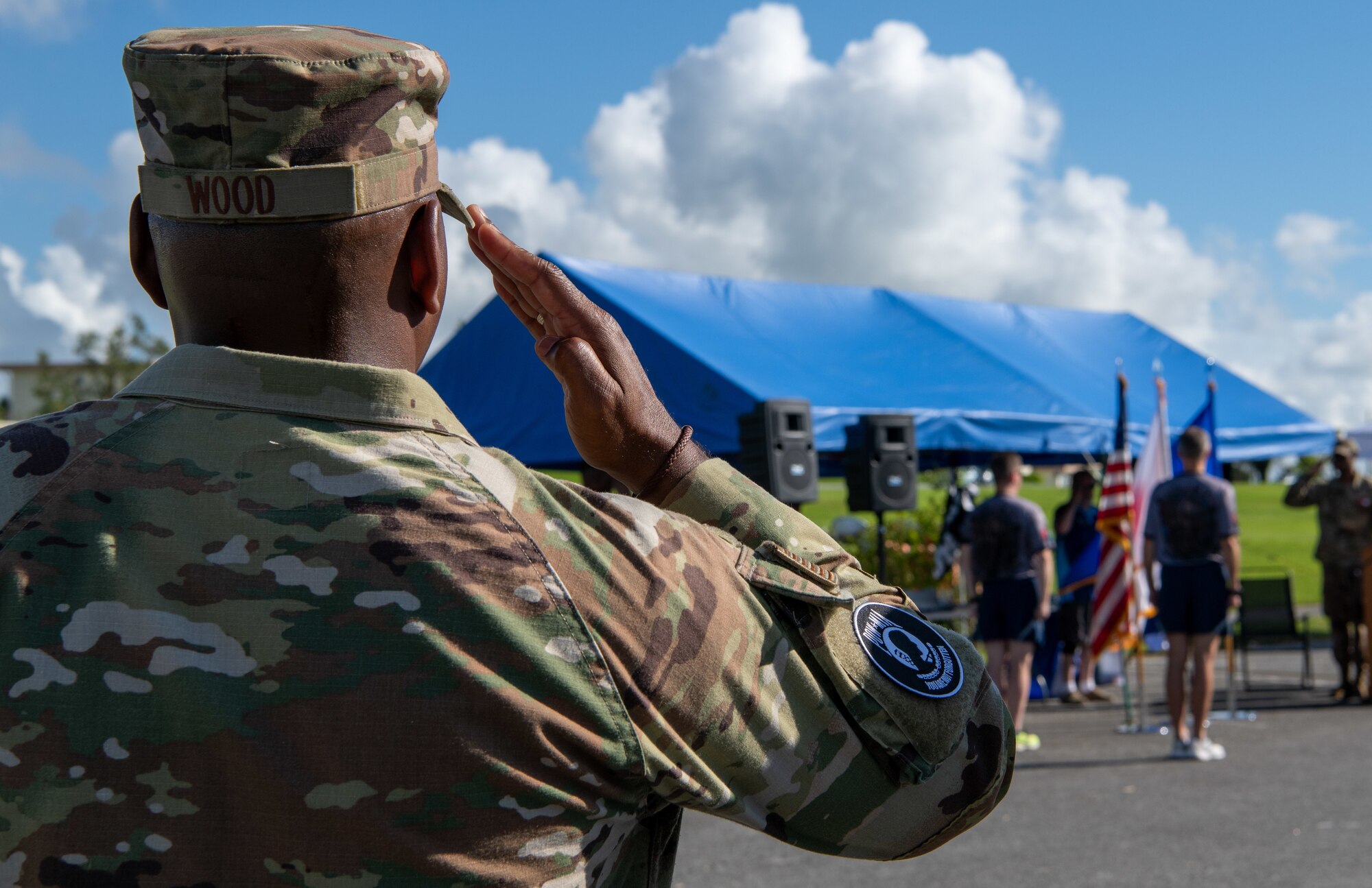 An Airman wearing a POW/MIA patch salutes the flags.