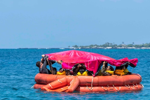 Airmen assemble a canopy over their heads while traveling through a body of water in a rubber raft.