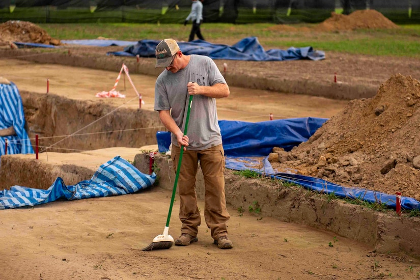 A man sweeps the dirt at the site of an excavation.