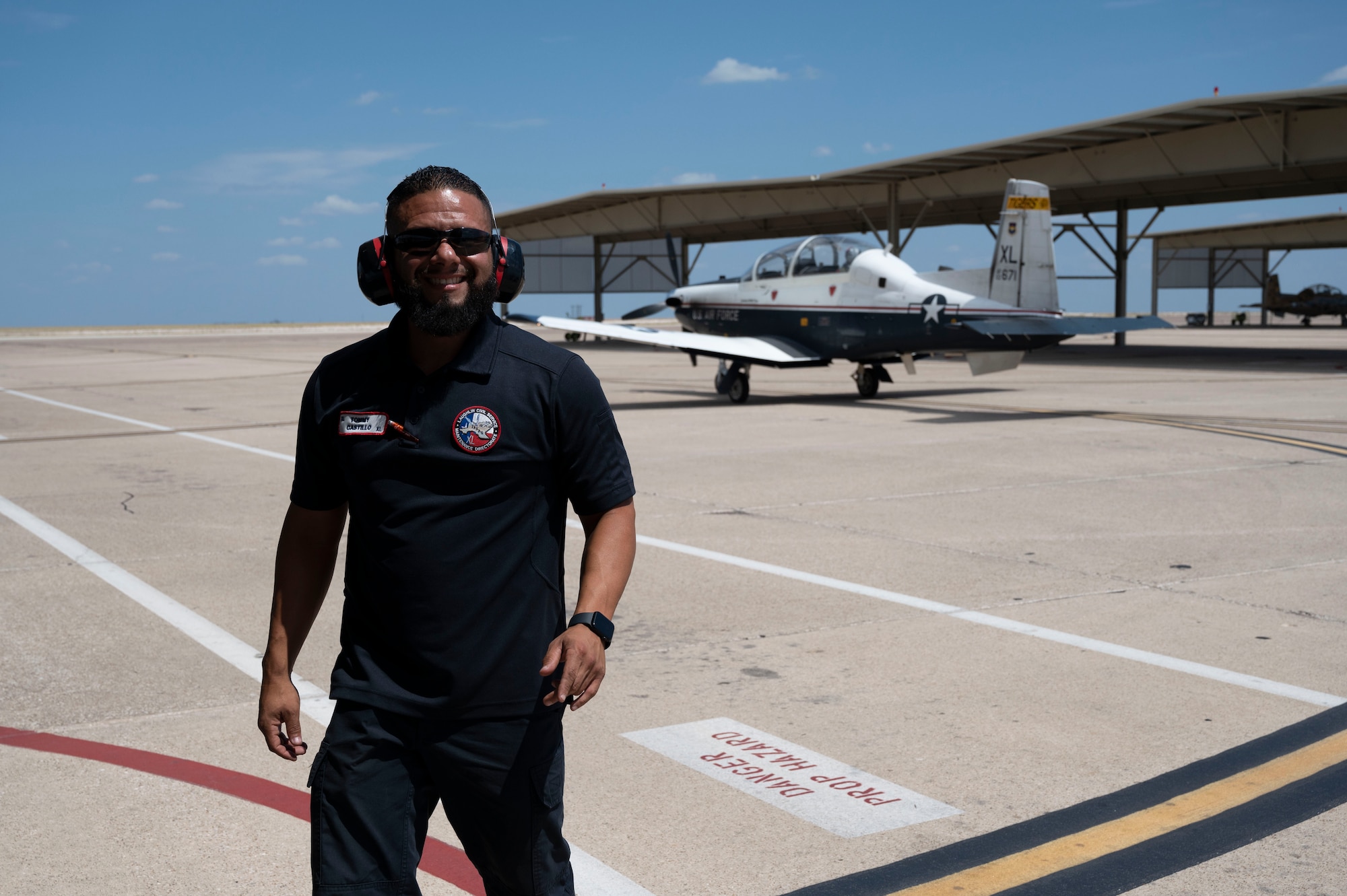 Tommy Castillo, 47th Maintenance Directorate T-6A Texan II crew chief, poses in front of a departing T-6A Texan II on the flight line at Laughlin Air Force Base, Texas, Sept. 11, 2023. Torres is a Del Rio native who works at Laughlin AFB to create the world’s best pilots. (U.S. Air Force photo by Airman 1st Class Kailee Reynolds)