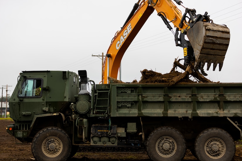 Alaska Army National Guardsmen, assigned to the 910th Engineer Support Company, assist one another by operating heavy machinery to dispose of any waste found at their construction site as a part of their annual training on Joint Base Elmendorf-Richardson, Alaska, Aug. 8, 2023.