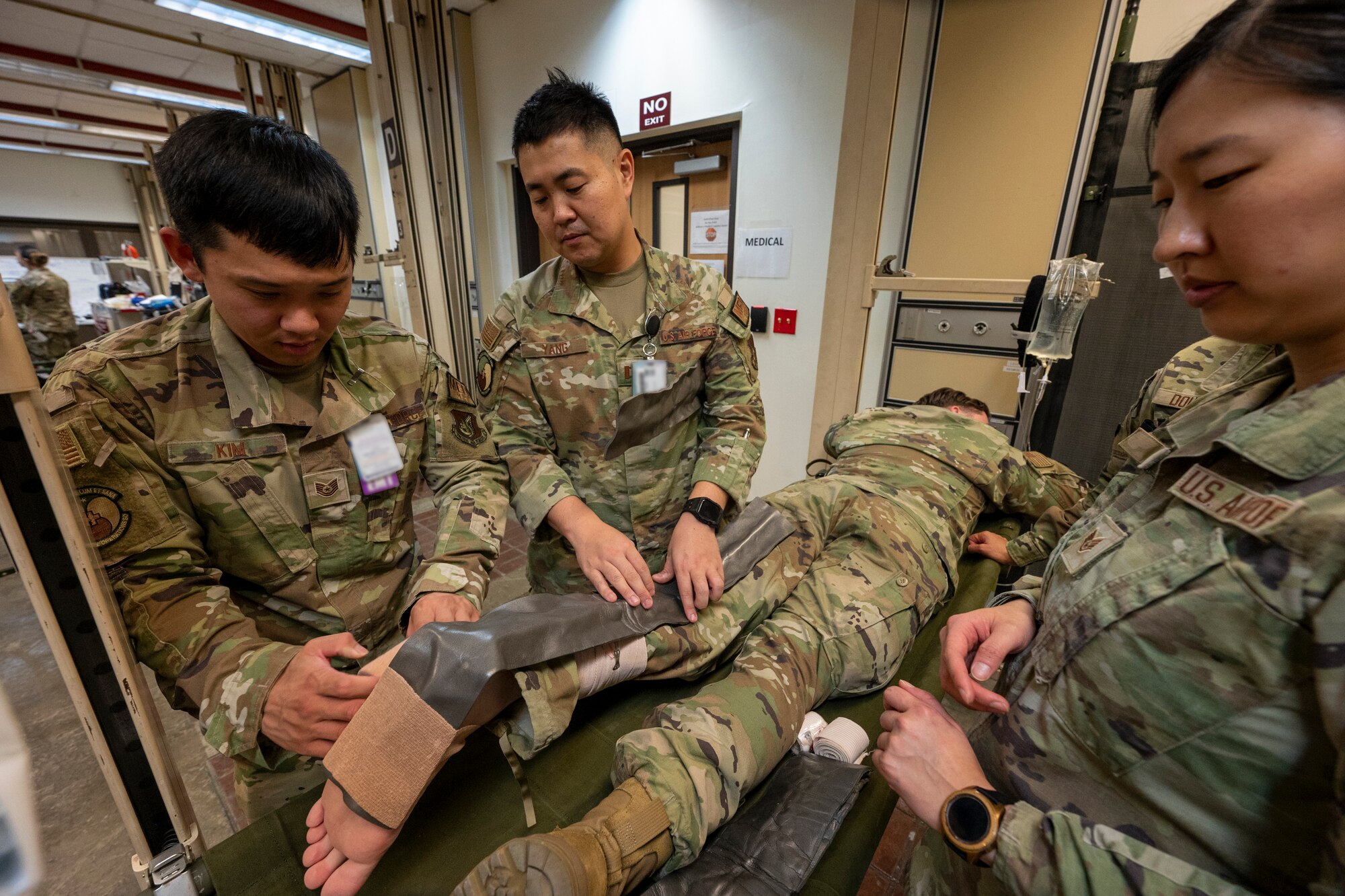 From the left, U.S. Air force Tech. Sgt. Edward Kim, medical surgical nursing unit noncommissioned officer in charge; Capt. Ji Yang, MSNU element lead; and Staff Sgt. Angelina Lee, allergy and immunization technician, all from the 51st Healthcare Operations Squadron, wrap a simulated patient's leg during a mass casualty training event at Osan Air Base, Republic of Korea, Sept. 21, 2023. MASCALs are situations in which a large number of casualties or injured individuals occur simultaneously, often as a result of a single incident or event, such as natural disasters, terrorist attacks, military engagements or major accidents. If not properly prepared, MASCALs can overwhelm medical resources; they require specialized training and protocols to effectively manage and treat the injured. The medics prepare daily for any contingencies if and when they occur, with the priority being ready to fight tonight. (U.S. Air Force photo by Senior Airman Aaron Edwards) (This photo has been altered for security purposes by blurring out identification badges.)