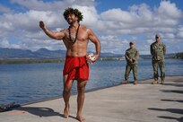 Louis Santos, extends his right arm to the left of the frame while holding a conch shell on his left hip, as he performs a traditional Hawaiian oli (chant) to bless the land, asking for protection and to foster good energy, during a Hawaiian blessing ceremony held at the water front of Pearl Harbor, as ceremony attendees look on.
