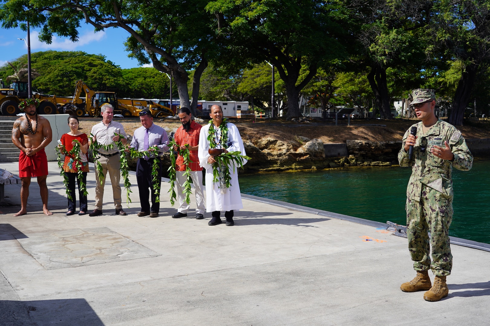 Capt. Steve Padhi, right, Officer in Charge of Construction Pearl Harbor Naval Shipyard, addresses the crowd at the dry dock blessing ceremony held at the water front of Pearl Harbor, as ceremony participants holding maile lei look on.
