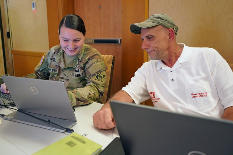 A man and a woman in an Army uniform look at information on a computer