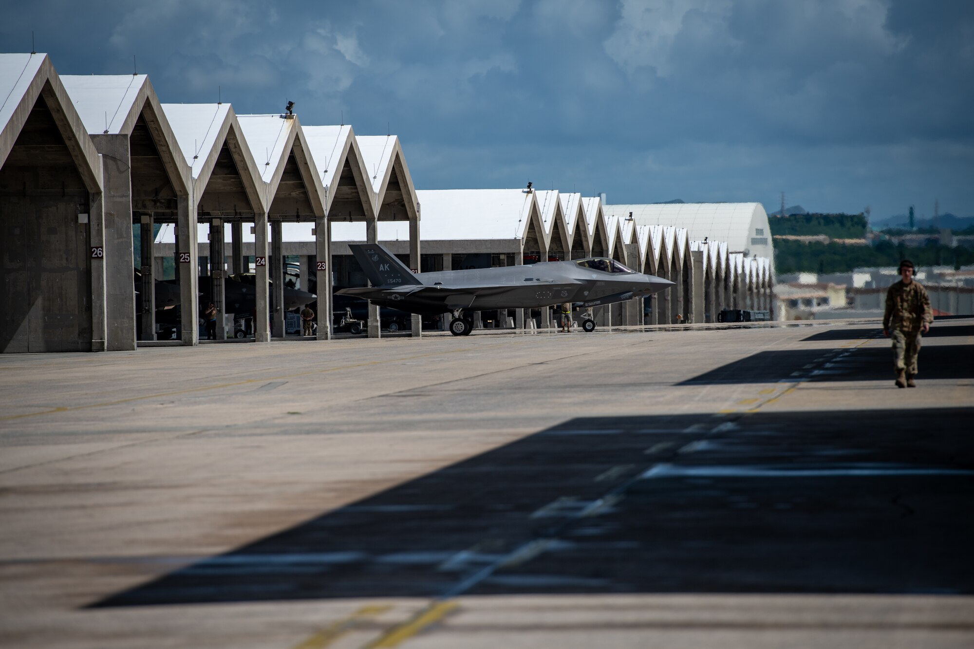 An Airman walks down a row of covered parking spots full of fighter jets