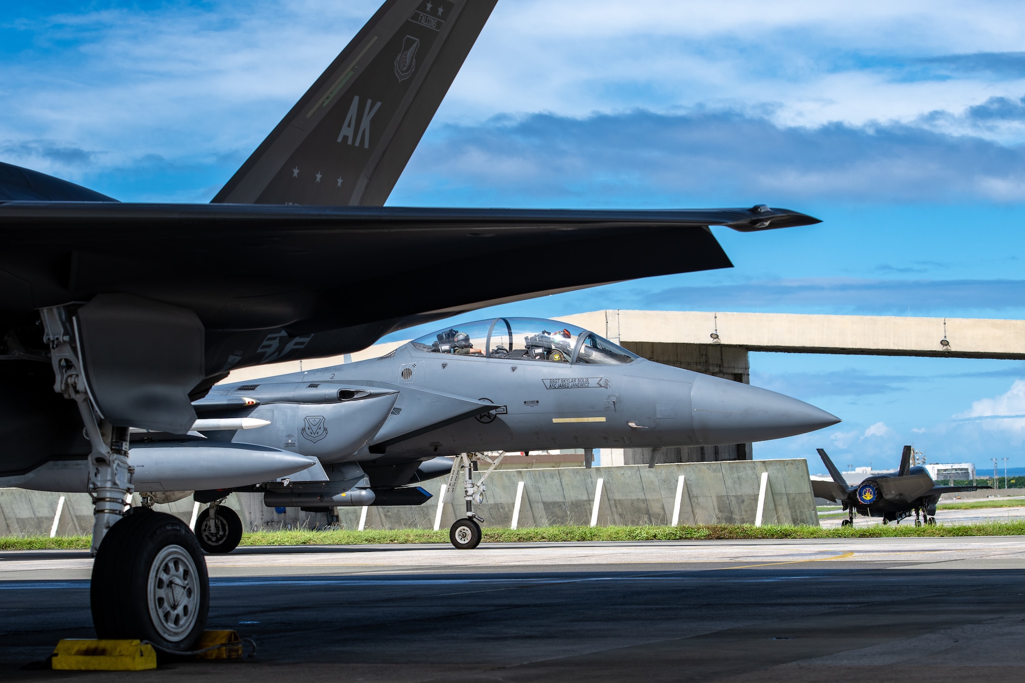 An F-15C taxis between two other fighter jets. The photo is taken from a low angle.
