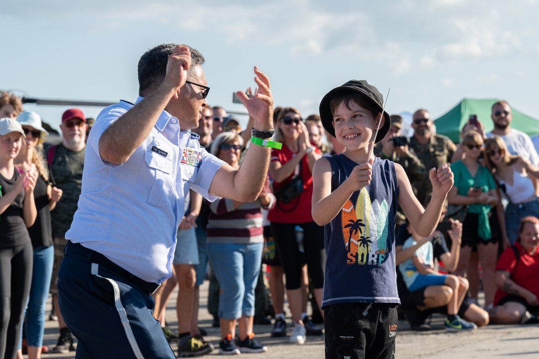 U.S. Air Force Maj. Rafael F. Toro-Quiñones, U.S. Air Forces in Europe Band commander and conductor, shows a Czech child how to conduct the band during a performance during the NATO Days event at Leoš Janáček Airport in Ostrava, Czech Republic, Sept. 16, 2023. The USAFE Band serves as a bridge to increase cultural ties and enrich the partnerships between the U.S. and Czech Republic through music. (U.S. Air Force photo by Airman 1st Class Christopher Campbell)