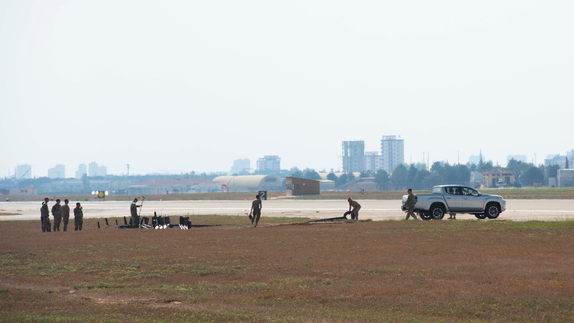 U.S. Airmen install machinery next to a runway. Buildings of the city of Adana are in the background.
