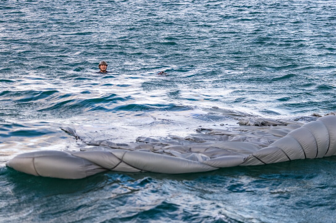 A Marine floats in the water next to a large parachute.