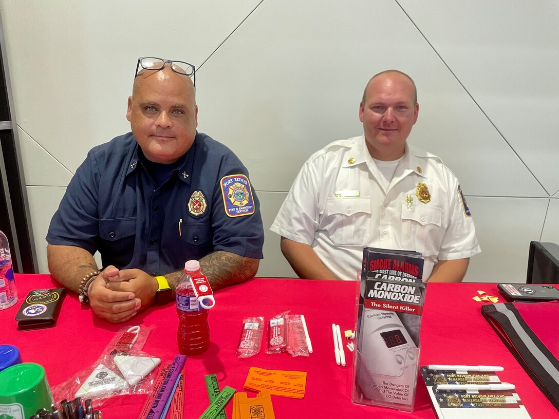 Two firefighters sit at a table that has information about fire safety.