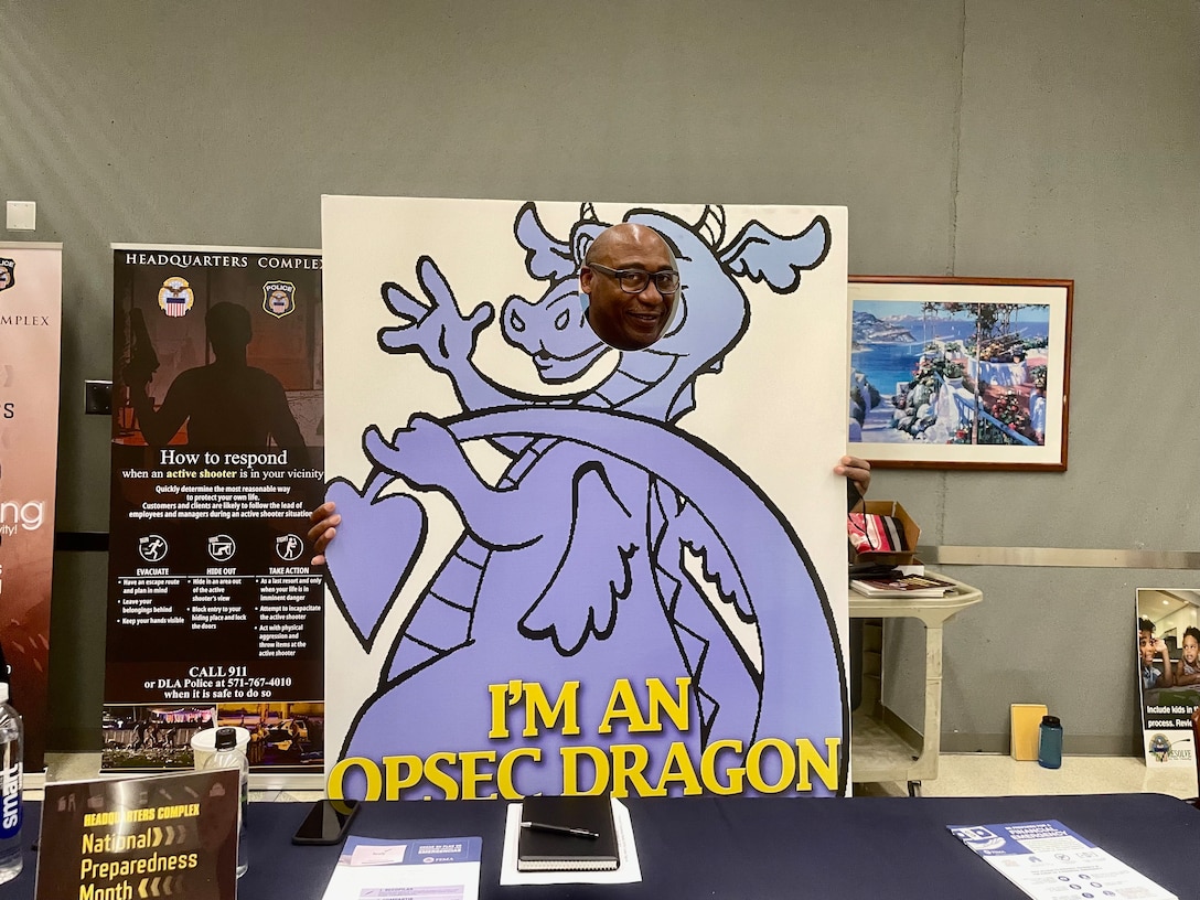 A man poses behind a photo of a dragon with his face in place of the dragon's face.
