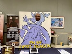 A man poses behind a photo of a dragon with his face in place of the dragon's face.