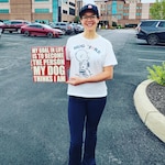 Woman holding a sign that reads My Goal In Life Is to Become The Person My Dog Thinks I Am.