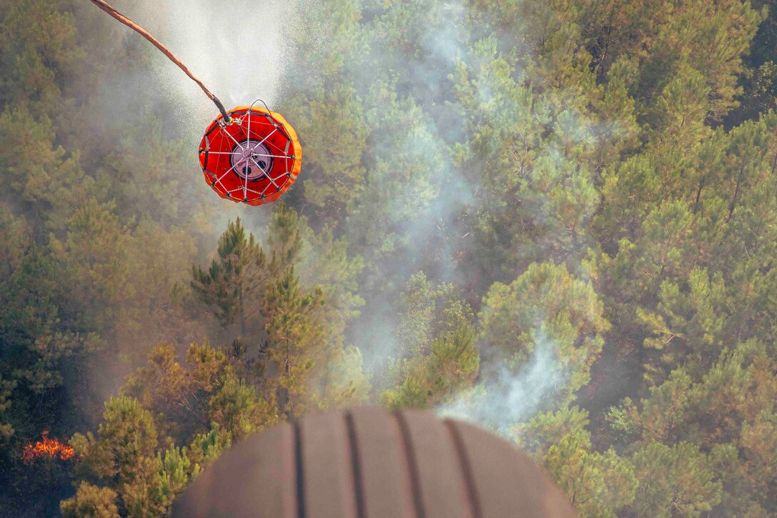 A bucket carries water over smoldering trees.