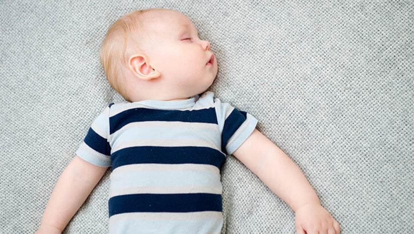 A baby lies on his back on an uncluttered mattress.