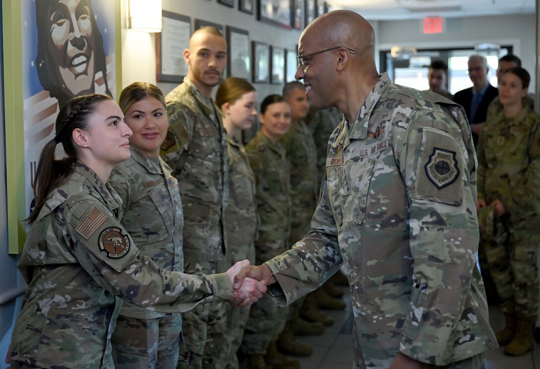 An Air Force general shakes hands with an airman standing in a row of airmen indoors.