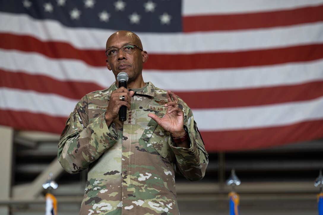 An Air Force general speaks in a microphone while standing in front of an American flag.