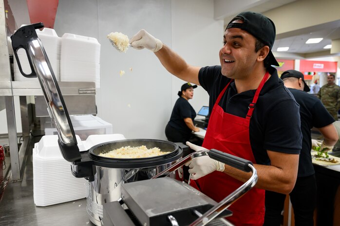 A food worker flashes a wide smile as he scoops rice