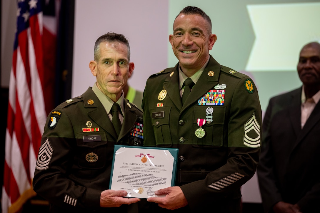 Two Army Soldiers pose for a photo holding an written citation award.