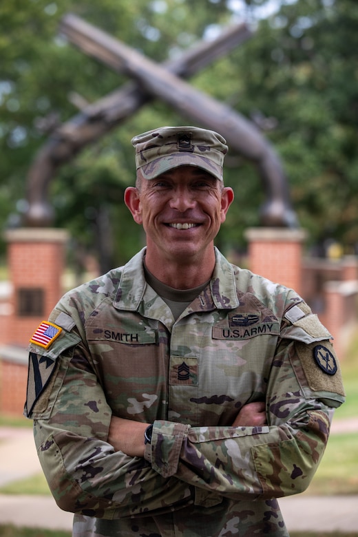 An Army Soldier poses for a photo in front cross rifles in the background, the symbol of the Army's Military Police.