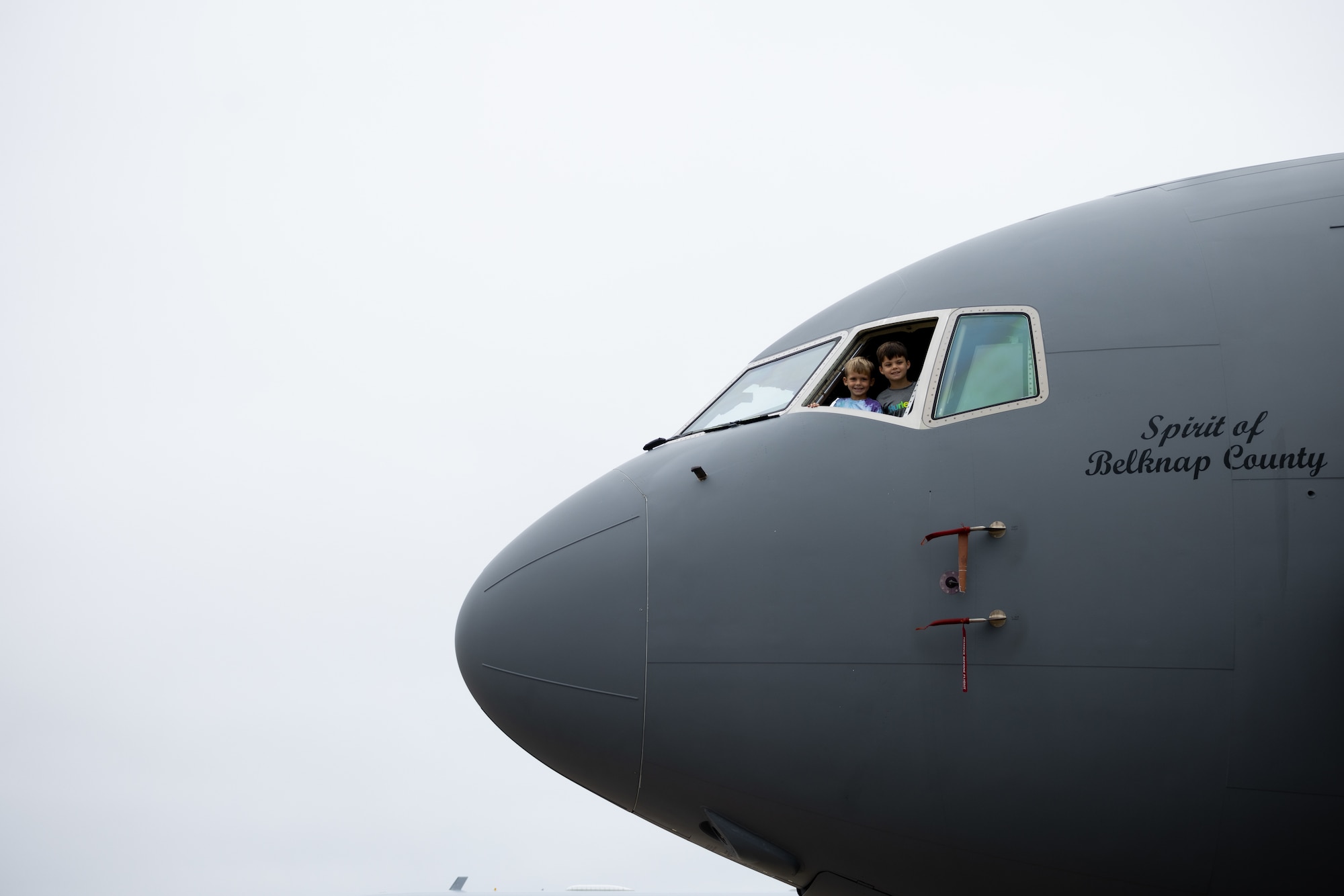 two children poke their heads out of the KC-46 cockpit window
