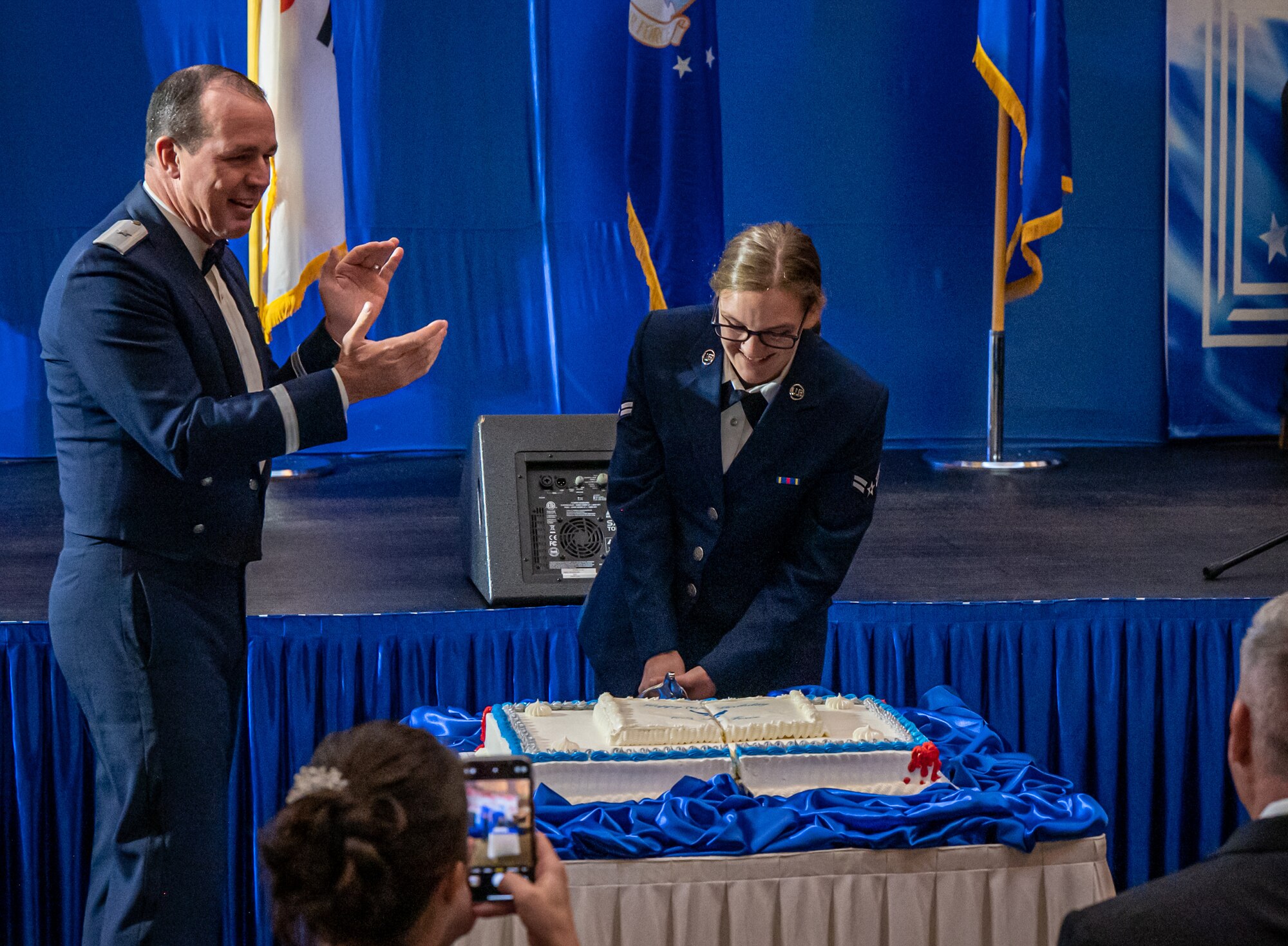 U.S. Air Force Brig. Gen. Steven Gorski, Director of Intelligence United States Forces Korea, observes Airman 1st Class Skye Lavalley, the youngest Airmen in attendance of the Air Force Ball, cut the birthday cake at U.S. Army Garrison Yongsan, Republic of Korea, Sept. 23, 2023. The most senior and junior Airmen traditionally cut the ceremonial cake to symbolize the passing of heritage between generations. (U.S. Air Force photo by Staff Sgt. Kelsea Caballero)