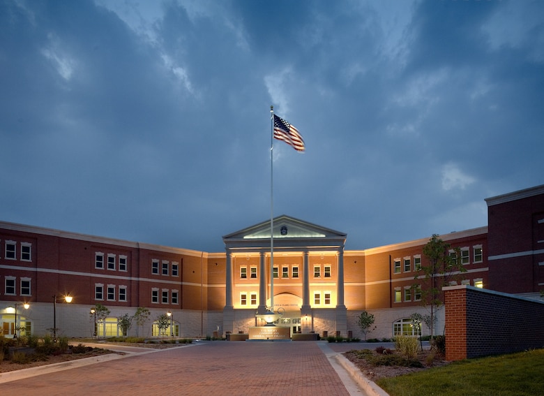 A building is seen at dusk with an American flag and a grey sky in the background.