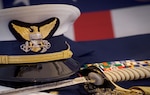 A Coast Guard officer's cover, sword, gloves, and ribbons are displayed together with the American Flag.