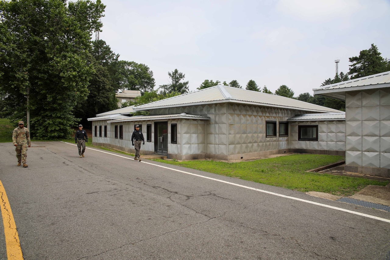 U.S. and foreign soldiers walk along a road next to buildings.