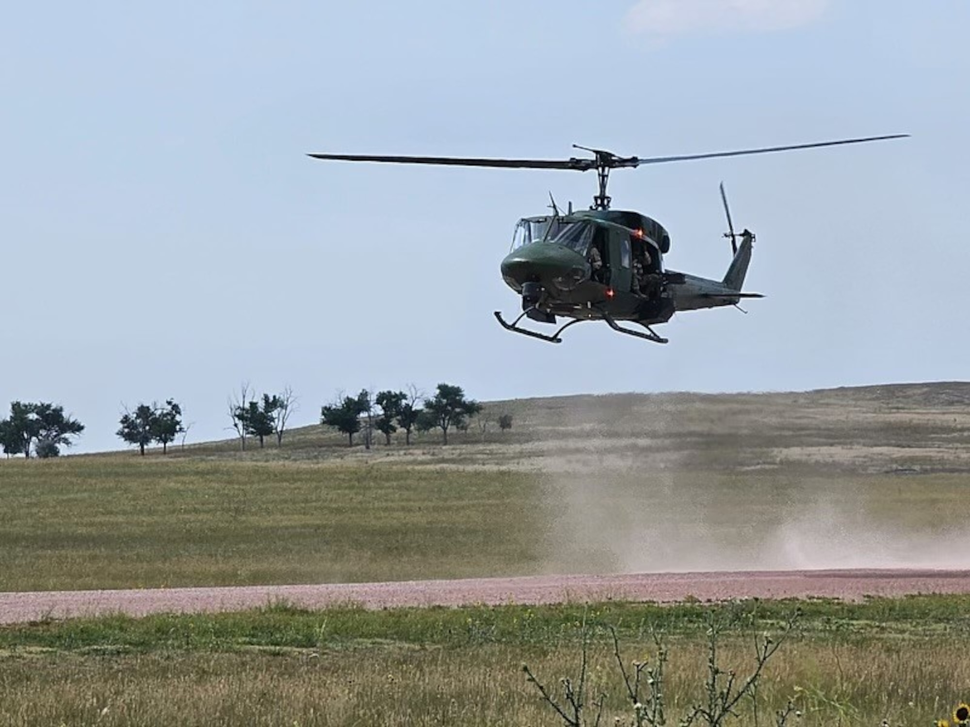A UH-1 Huey lands on brown dirt.
