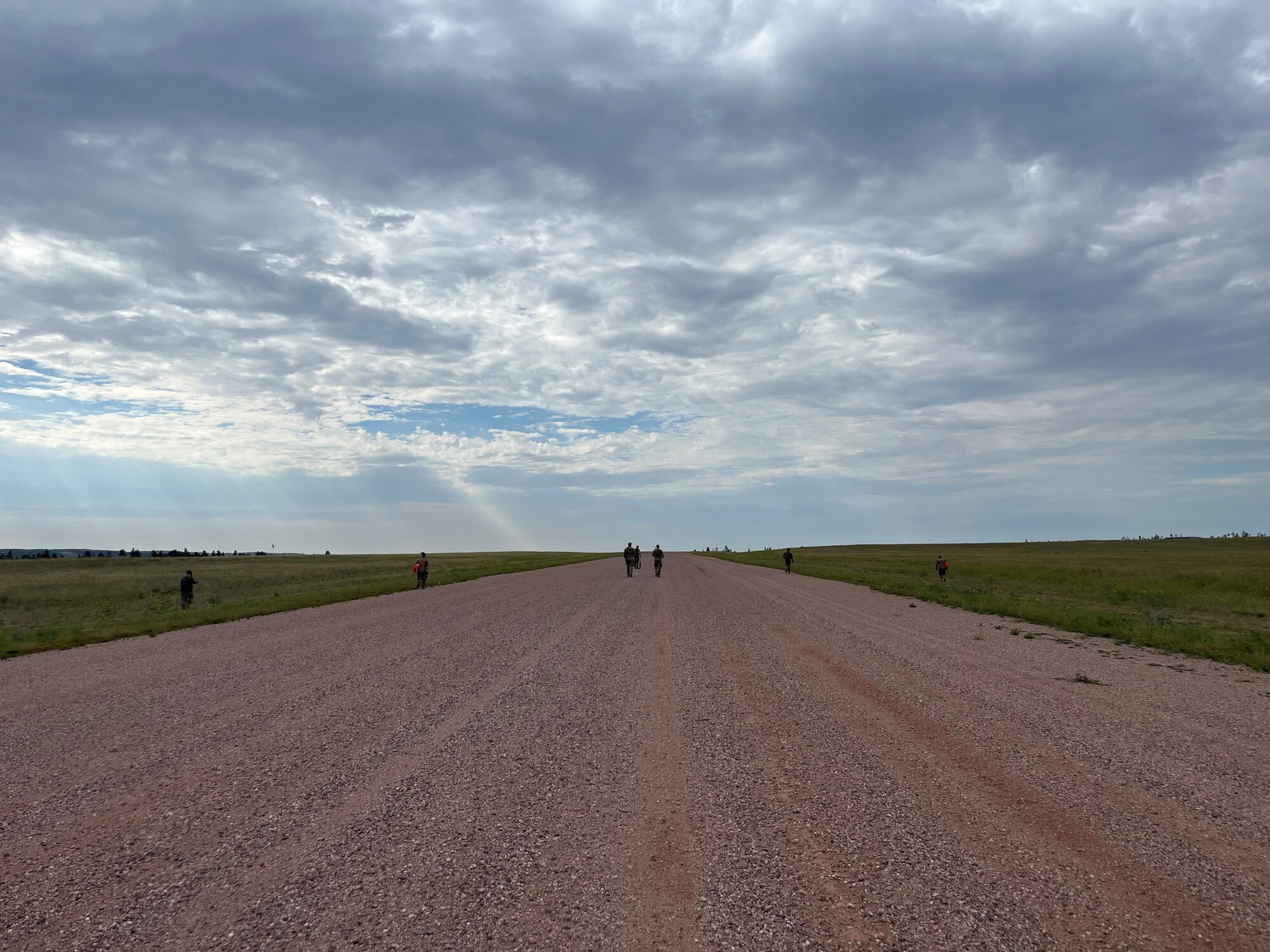 Two people walk on red gravel beneath a blue sky.