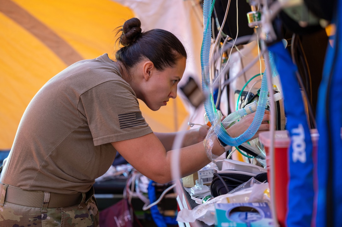 An airman works handles wires and tubes on a medical device.