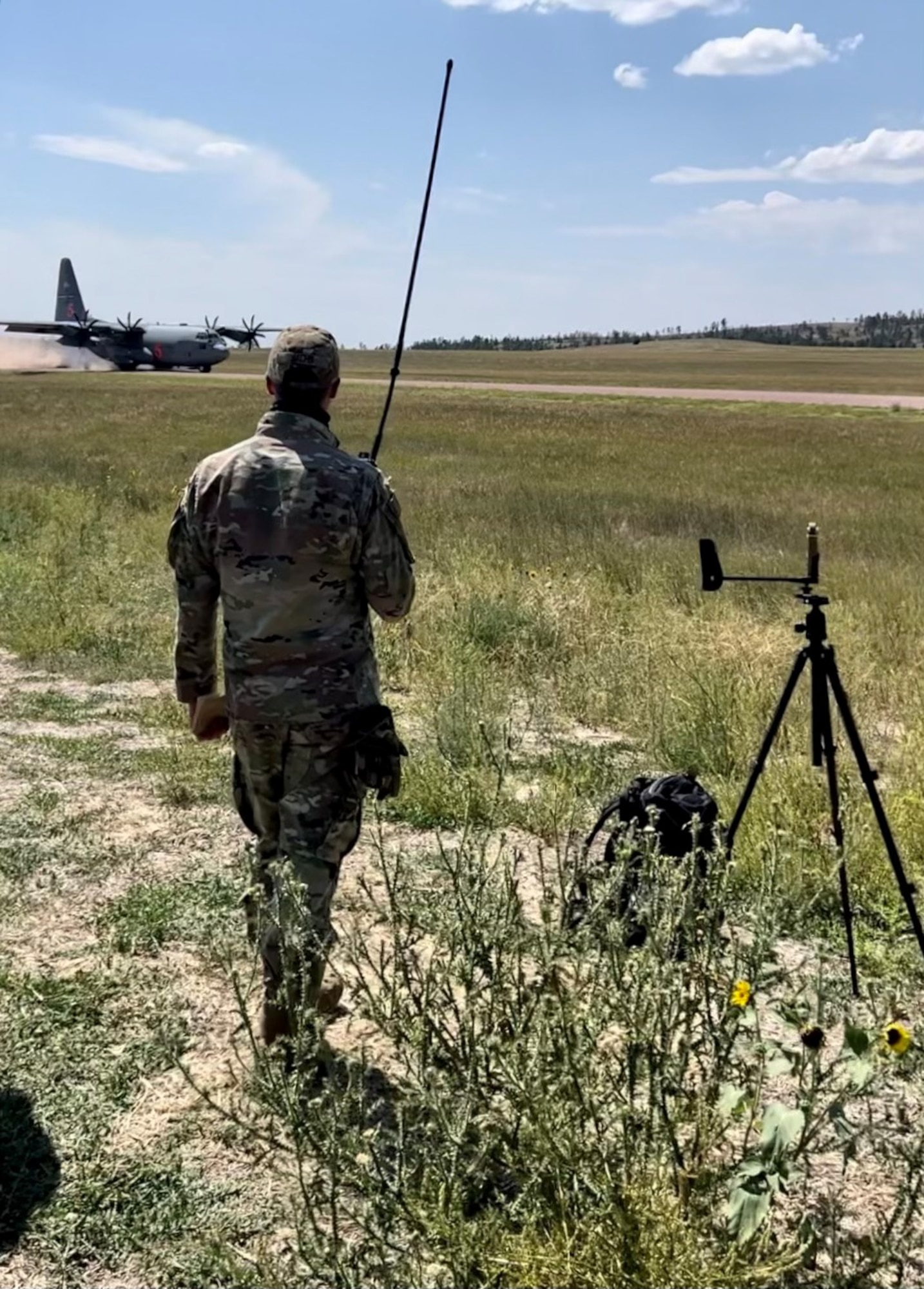 A person in a green uniform talks on a radio in front of a C-130 aircraft.