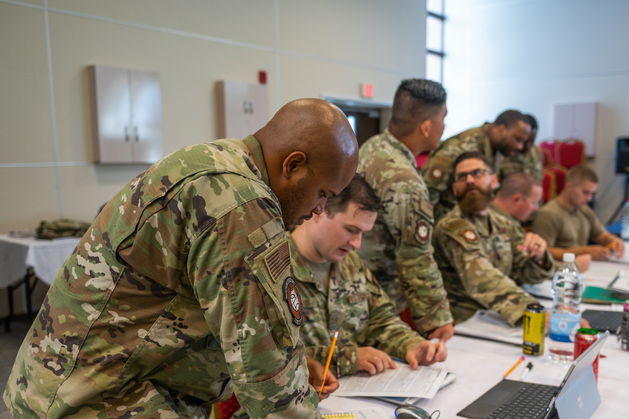 Airmen sit at table with worksheets and computers
