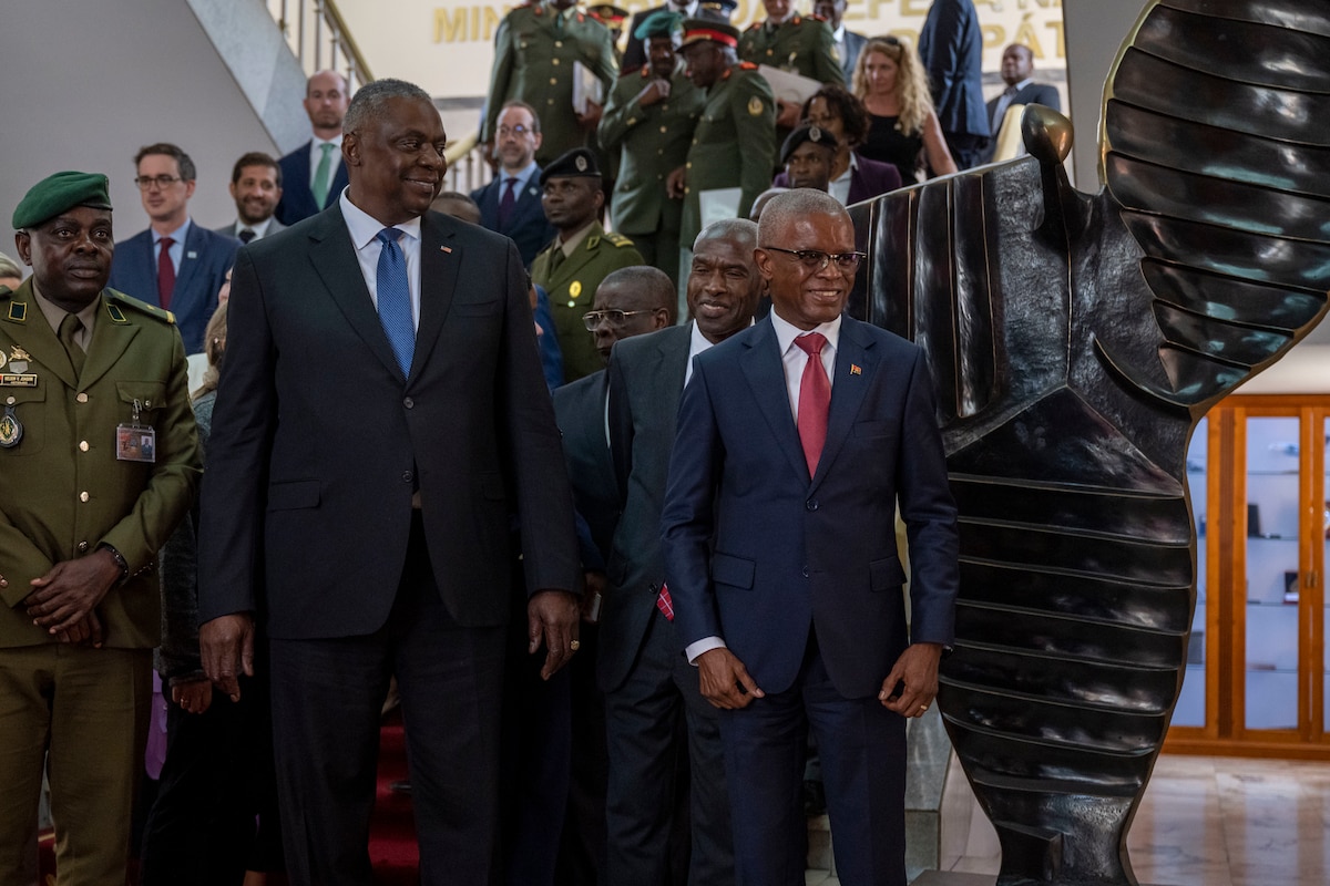 Two people in business suits walk side-by-side, smiling, as others walk behind them.