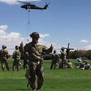 Man wearing U.S. Army uniform stands in front of a group of U.S. Army soldiers and a helicopter.