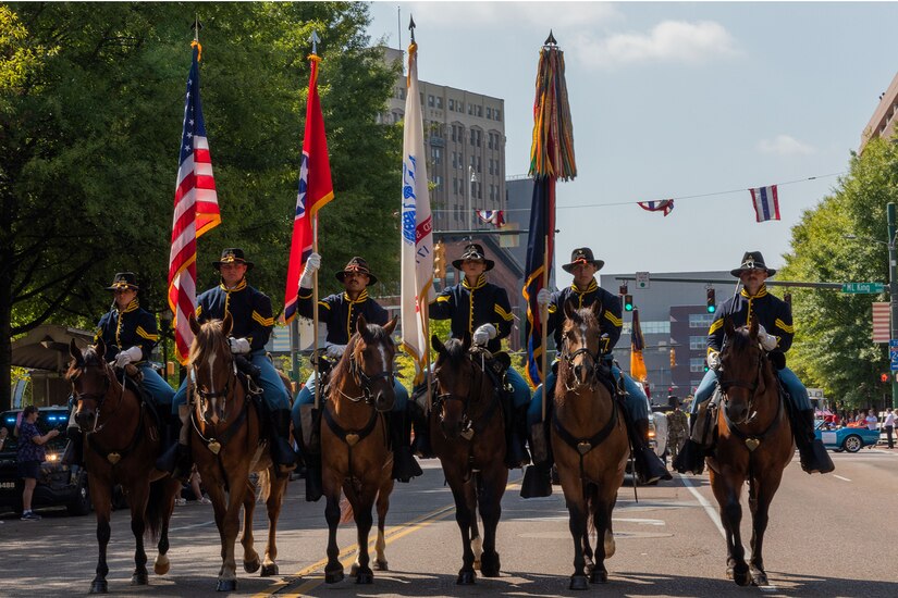 Service members on horseback line the street for a parade.