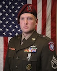 Man in U.S. Army uniform standing in front of an American Flag