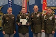 Four men wearing U.S. Army uniforms posing for a the award recognition of one of the men.