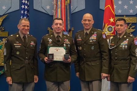Four men wearing U.S. Army uniforms posing for a the award recognition of one of the men.