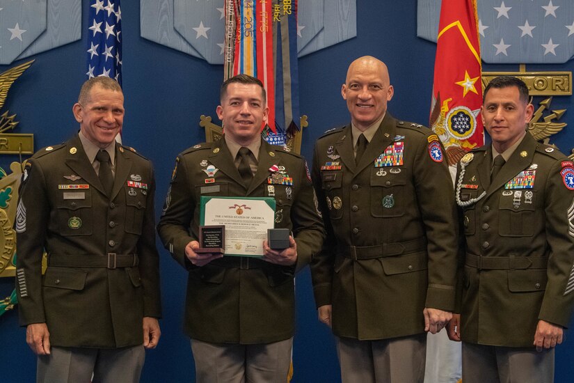 Four men wearing U.S. Army uniforms posing for a the award recognition of one of the men.