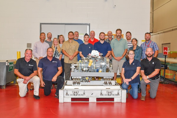 Fleet Readiness Center East (FRCE) and Rolls Royce personnel pose for a group photo with a fully assembled lift fan clutch for the F-35B Lightning II aircraft. FRCE personnel became the first within the Department of Defense (DoD) to perform a successful assembly of this component outside of Rolls Royce’s LiftWorks facility in Indianapolis. (Photo by Joe Andes, Fleet Readiness Center East Public Affairs)