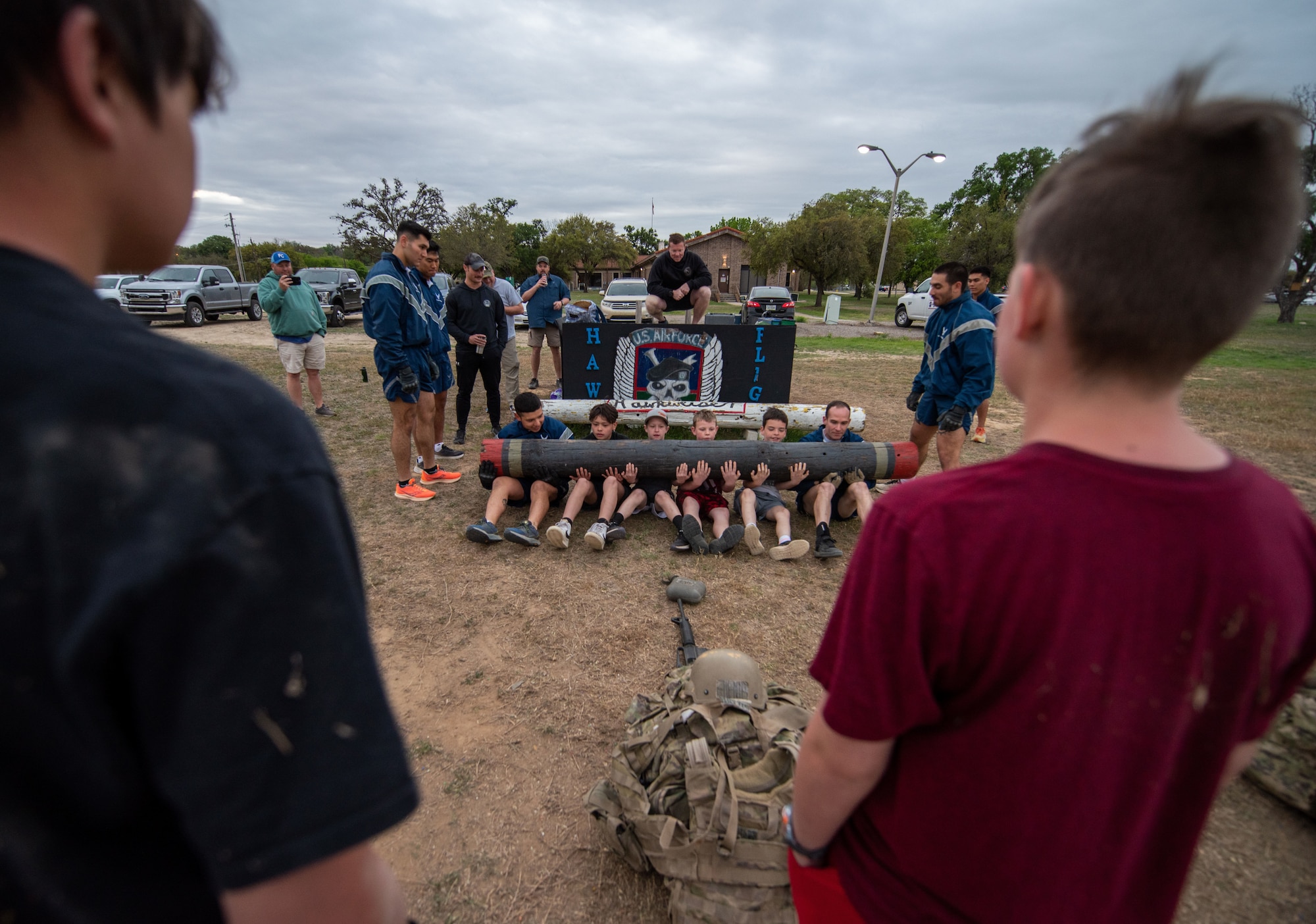 Two Tactical Air Control Party students assist a few Boy Scouts  in weight bearing sit-up exercises with a large log.