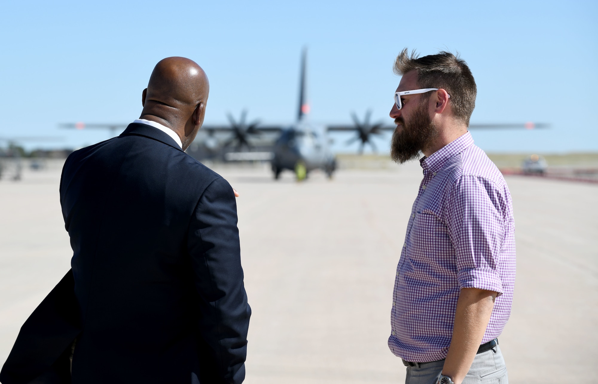 Two gentlemen observe a C-130H Hercules as it taxis off the ramp at Peterson Space Force Base.