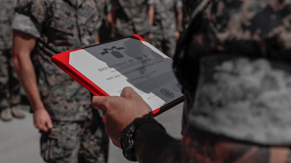U.S. Marine Corps Sgt. Maj. Christian Appleman, sergeant major of 2d Battalion, 8th Marine Regiment, 2d Marine Division, reads a Navy and Marine Corps Achievement Medal for Navy Petty Officer 3rd Class Clay Campbell, a field medical technician with 2d Battalion, 8th Marine Regiment, 2d Marine Division, on Camp Lejeune, North Carolina, September 15, 2023. Campbell was awarded and recognized for providing medical care to a young woman having a seizure until medics arrived on scene, ultimately saving her life. (U.S. Marine Corps photo illustration by Cpl. Megan Ozaki)