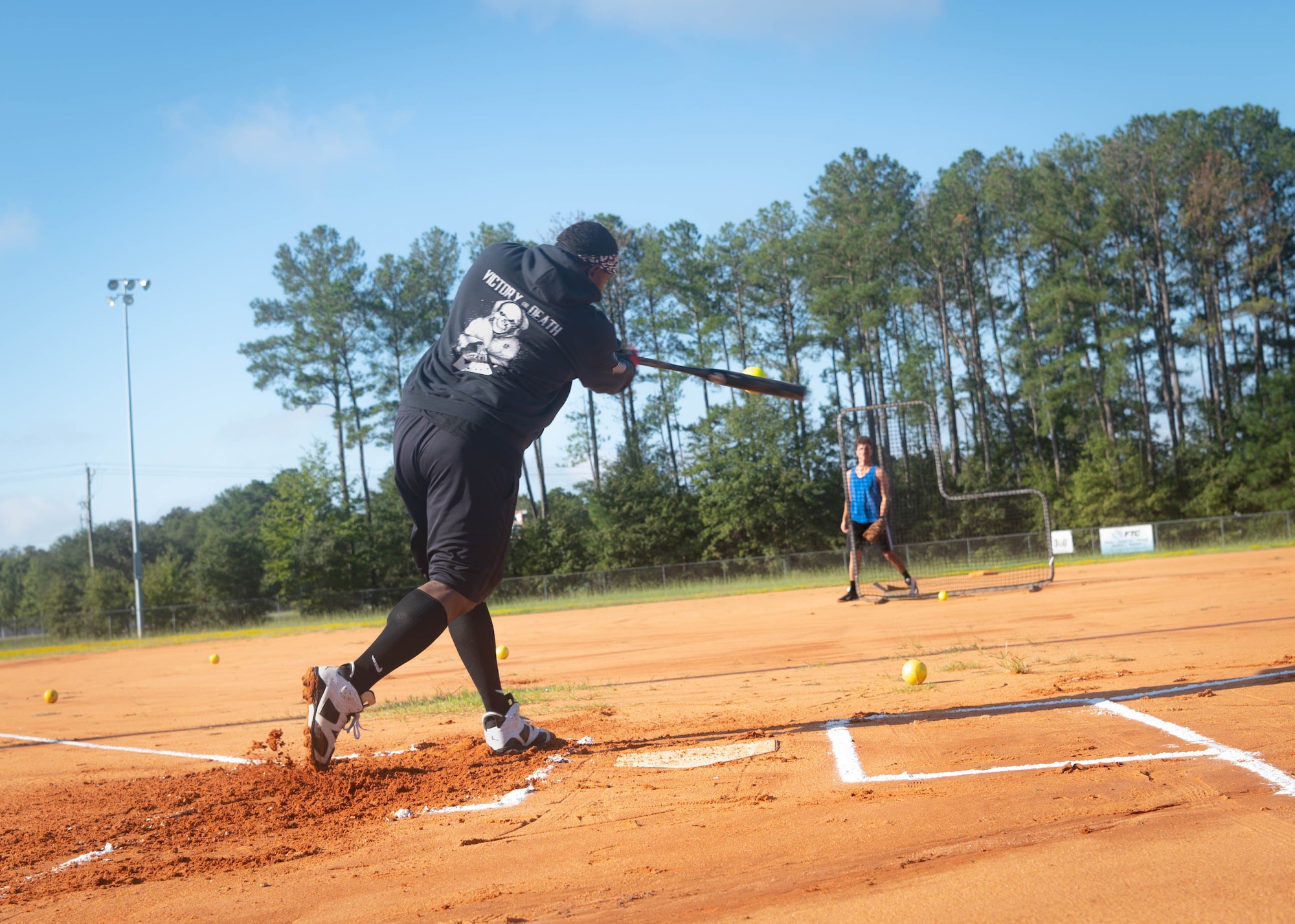Man swings a bat at a softball pitched by his teammate.