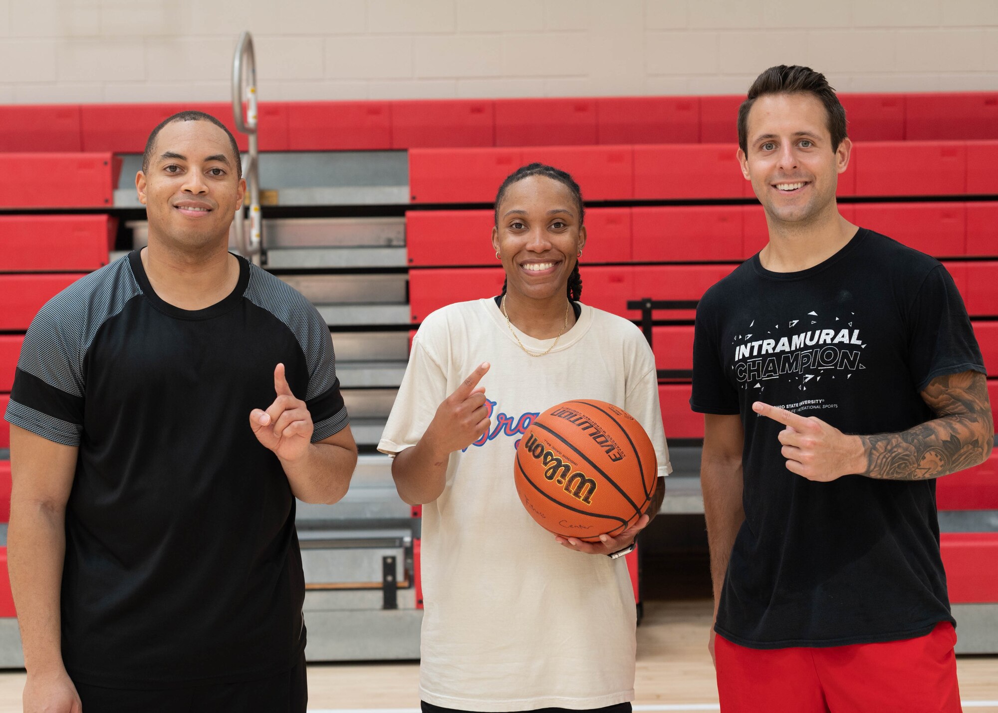 Three people pose in a gymnasium recognizing their victory in a 3 vs 3 basketball tournament.