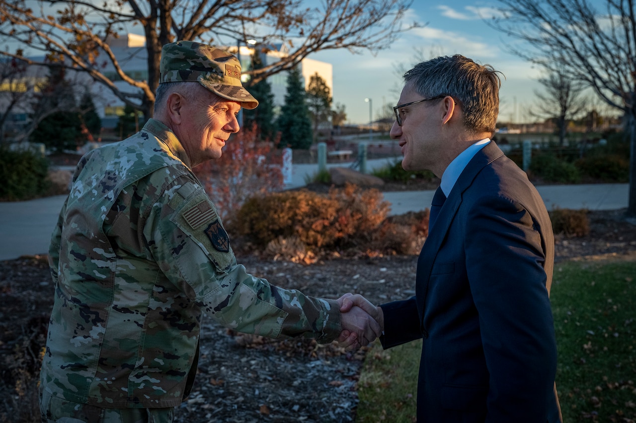 A man in uniform shakes hands with a man in civilian attire.